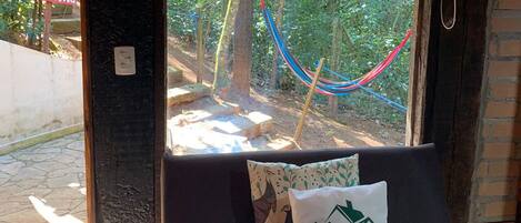 A window seat with a hammock, a pillow with a logo, and a neon sign outside.