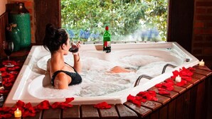 Une femme se détend dans un bain à remous, entourée de verdure, avec des pétales de rose et des bougies.