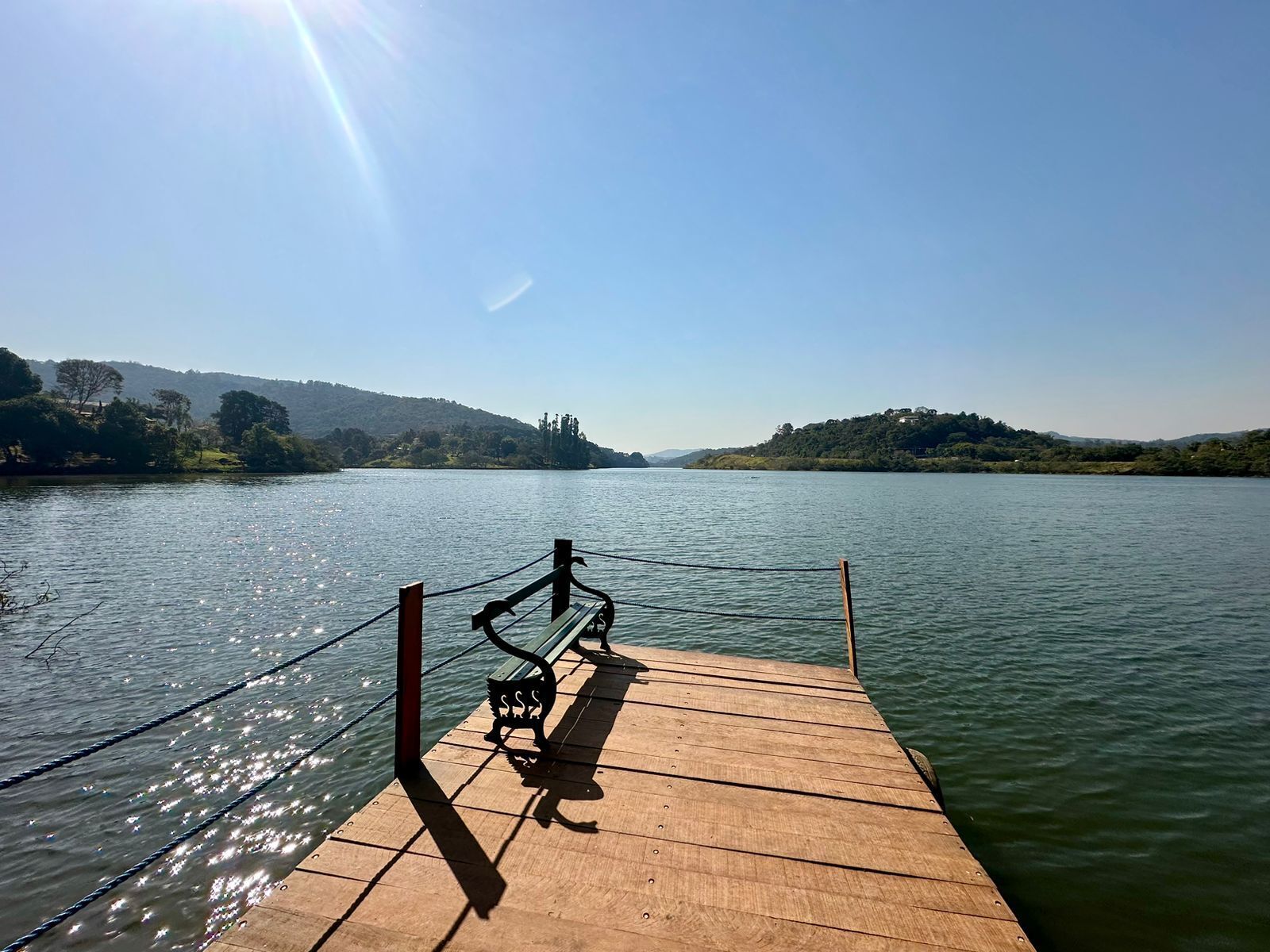 Un muelle de madera que se adentra en aguas tranquilas, con un banco y una barandilla metálica.
