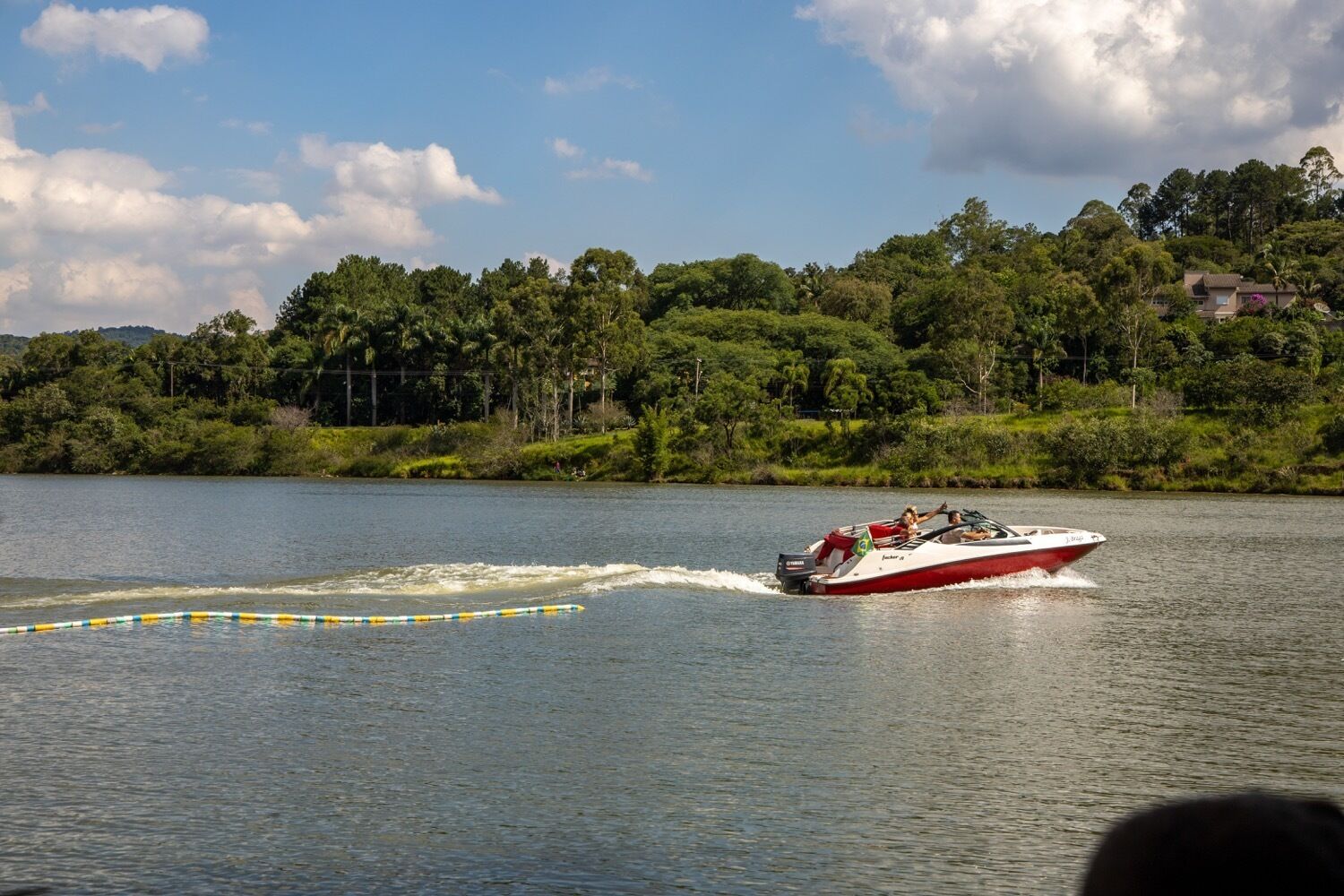 A speedboat on a lake with a forested shoreline and houses in the background.