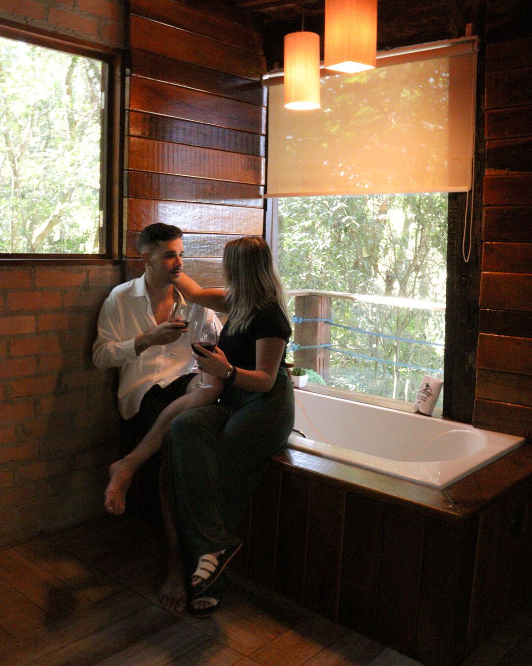 Ein Holzeinrichtung mit einer Badewanne, einem Fenster mit Blick ins Grüne und einer Hängelampe.