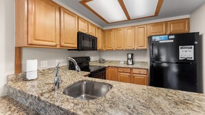 A kitchen with granite countertops, wooden cabinets, a stainless steel sink, a black refrigerator, and a microwave. - Condo in Copper's East Village w/ Balcony & Golf Course &Mountain Views! (Frisco)
