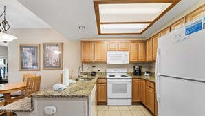 A kitchen with wooden cabinets, a white stove, a microwave, and a refrigerator. There is a dining table with chairs and a countertop with a sink. - Private Balcony w/ Golf Course & Slope Views, Short Walk to Shuttle Stop! (Copper Mountain)