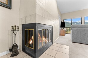 A modern living room with a fireplace, a television, and a view of mountains through large windows.