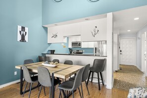 Ein Essbereich mit Holztisch, grauen Stühlen, einer Küche mit weißen Schränken und einer blauen Wand.