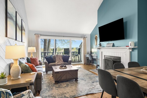 A living room with a sofa, coffee table, TV, fireplace, and dining area. - Venture Out at Shanty Creek Resort (Bellaire)