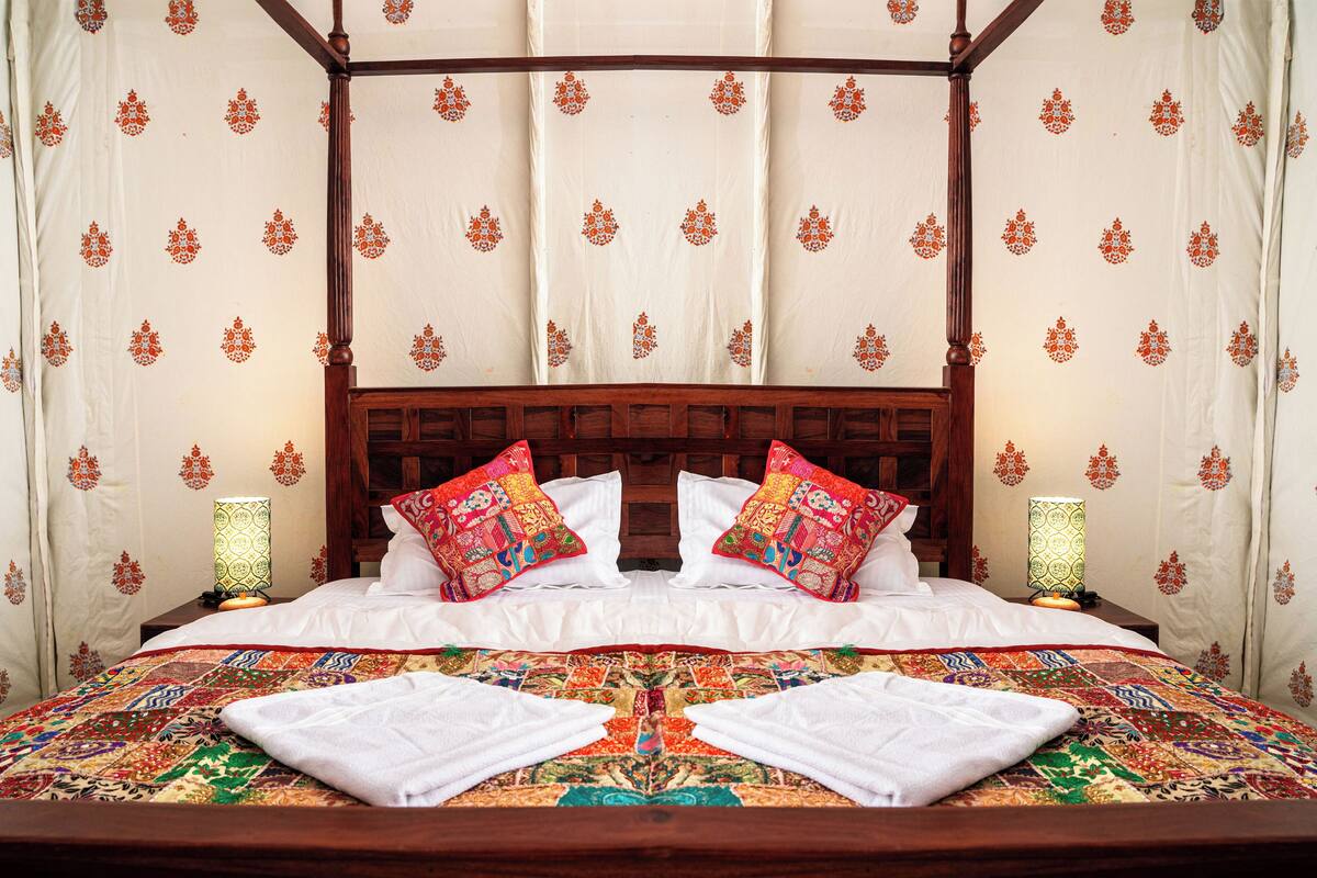 A four-poster bed with a colorful quilt, two pillows, and two bedside lamps.
