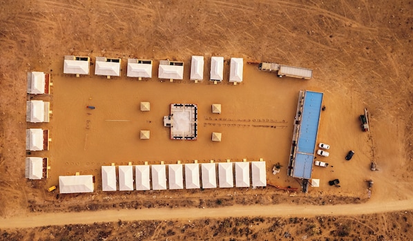 Vista aérea de un camping con varias tiendas de campaña, un edificio central y una estructura con techo azul.