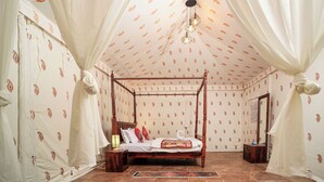 A four-poster bed with a wooden frame, white curtains, and patterned wallpaper.