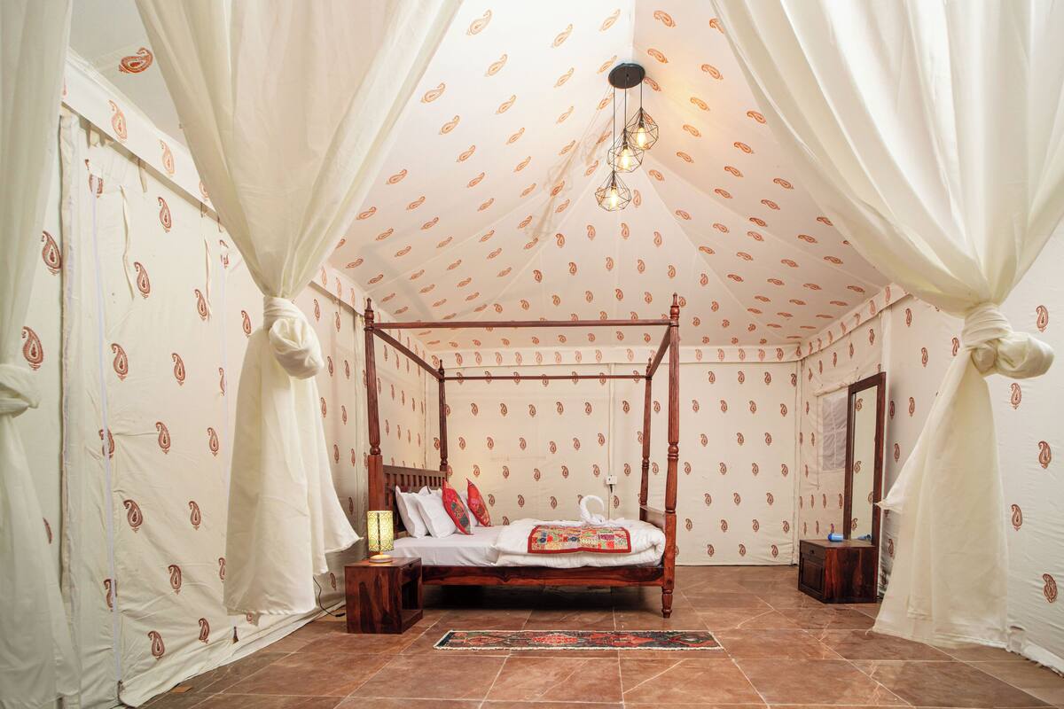 A four-poster bed with a wooden frame, white curtains, and patterned wallpaper.