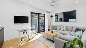 A modern living room with a flat-screen TV, a sofa, a coffee table, and a dining area with a glass table and chairs.