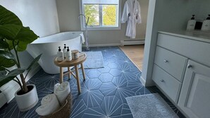 Een badkamer met een badkuip, wastafel, spiegel en een raam met uitzicht op bomen.