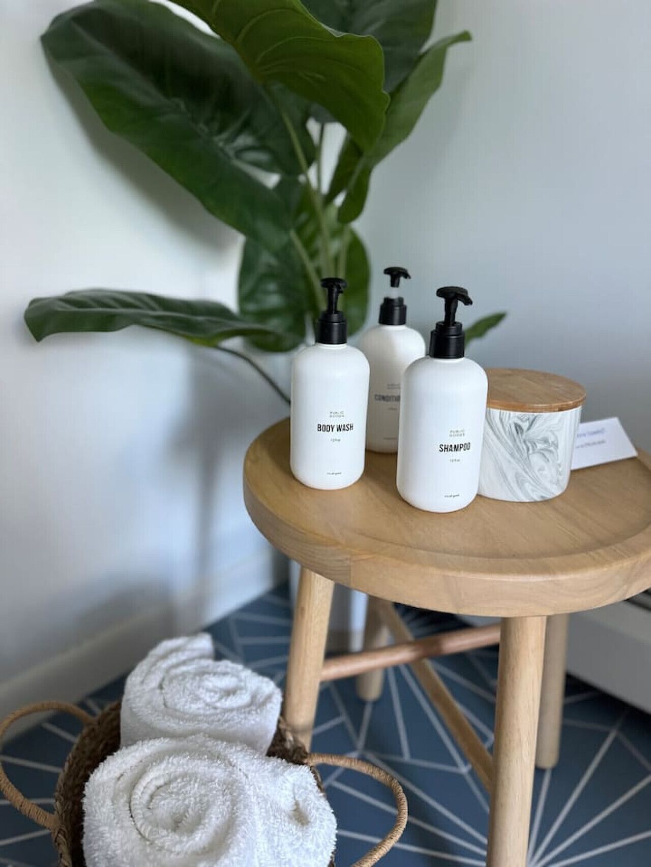 A small wooden table with three white bottles labeled "BODY WASH" and "SHAMPOO" and a white ceramic container with a marble design.