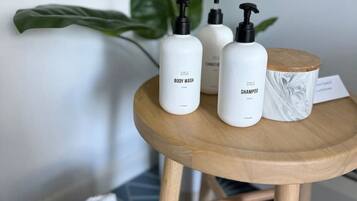 A small wooden table with three white bottles labeled "BODY WASH" and "SHAMPOO" and a white ceramic container with a marble design.