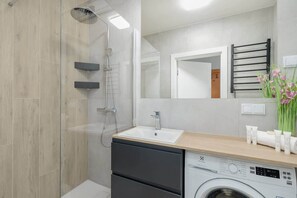 Un baño moderno con cabina de ducha de vidrio, lavabo, espejo, toallero y lavadora.