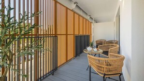 Un balcón con valla de madera, sillas de mimbre, una mesita redonda con una tetera y una planta en maceta.