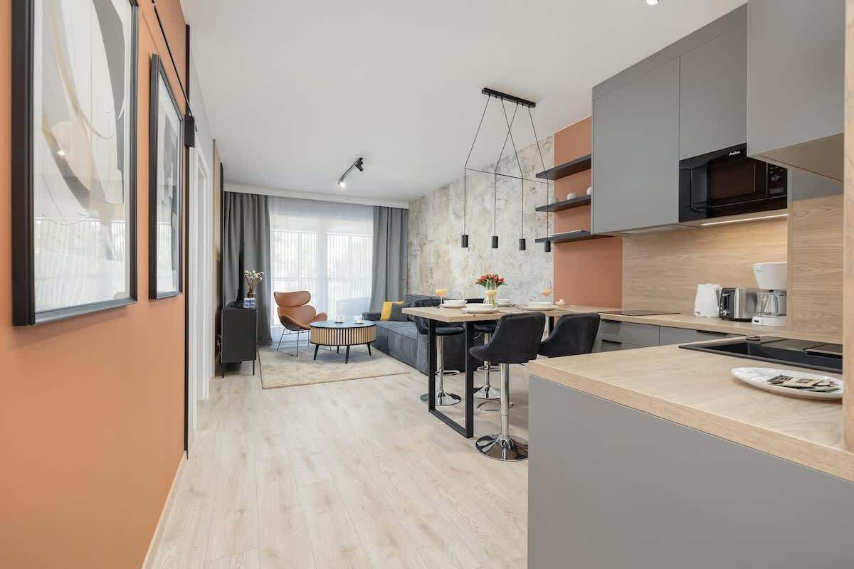 A modern kitchen with a central island, a dining area with a sofa and chairs, and a large window providing natural light.