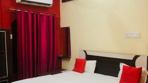 Une chambre d’hôtel avec un lit, des rideaux rouges, un téléviseur à écran plat et un appareil de climatisation.