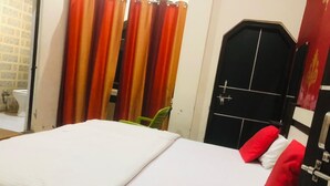 Une chambre d’hôtel avec un lit, des rideaux rouges et orange, une porte noire et un mur blanc.