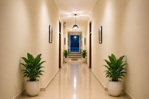 A hallway with two potted plants, framed pictures on the walls, and a staircase leading to a room with a blue door. - Holiday Beach Resort (Candolim)