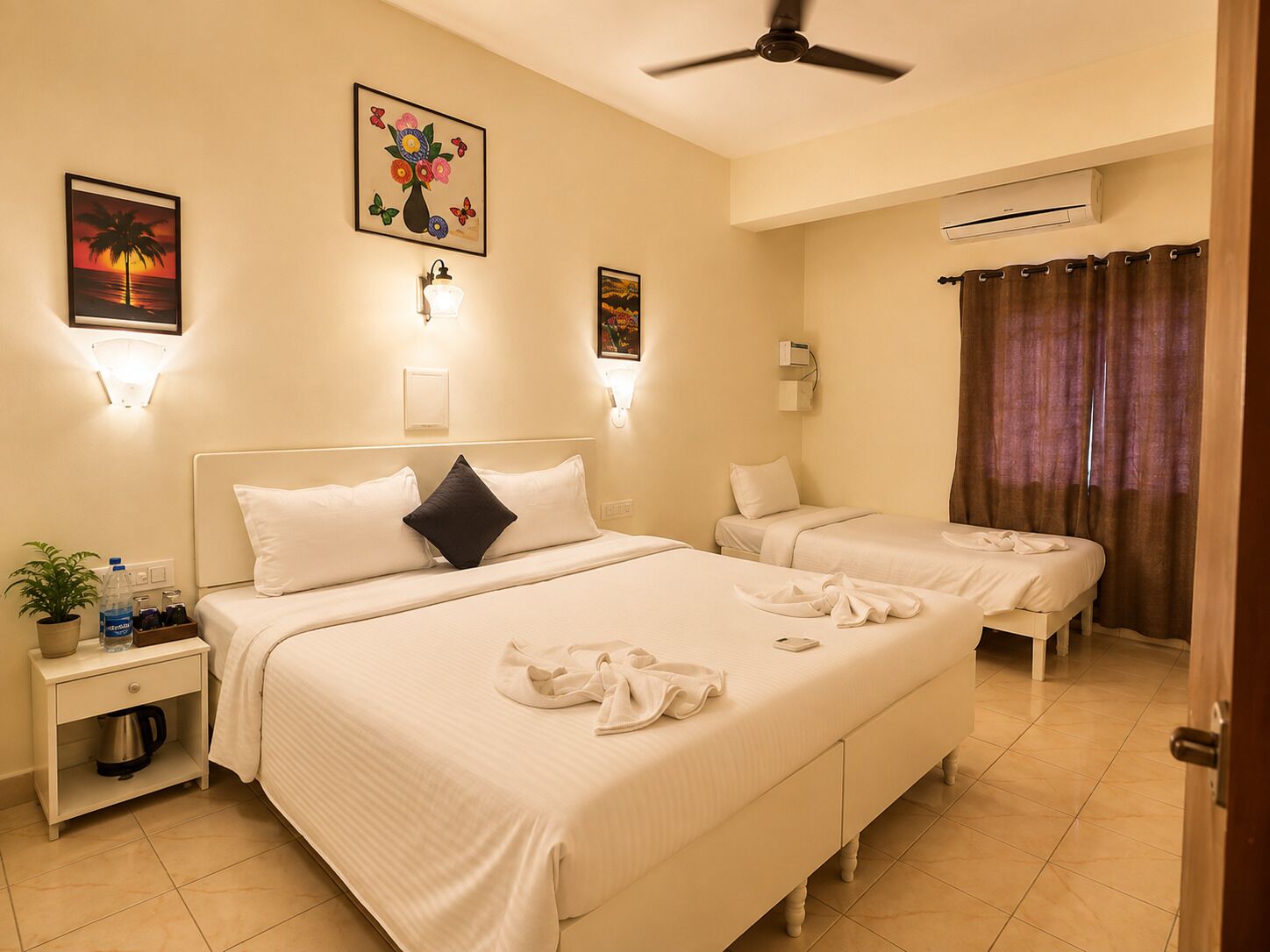 A hotel room with two beds, a ceiling fan, wall-mounted air conditioning, and artwork.