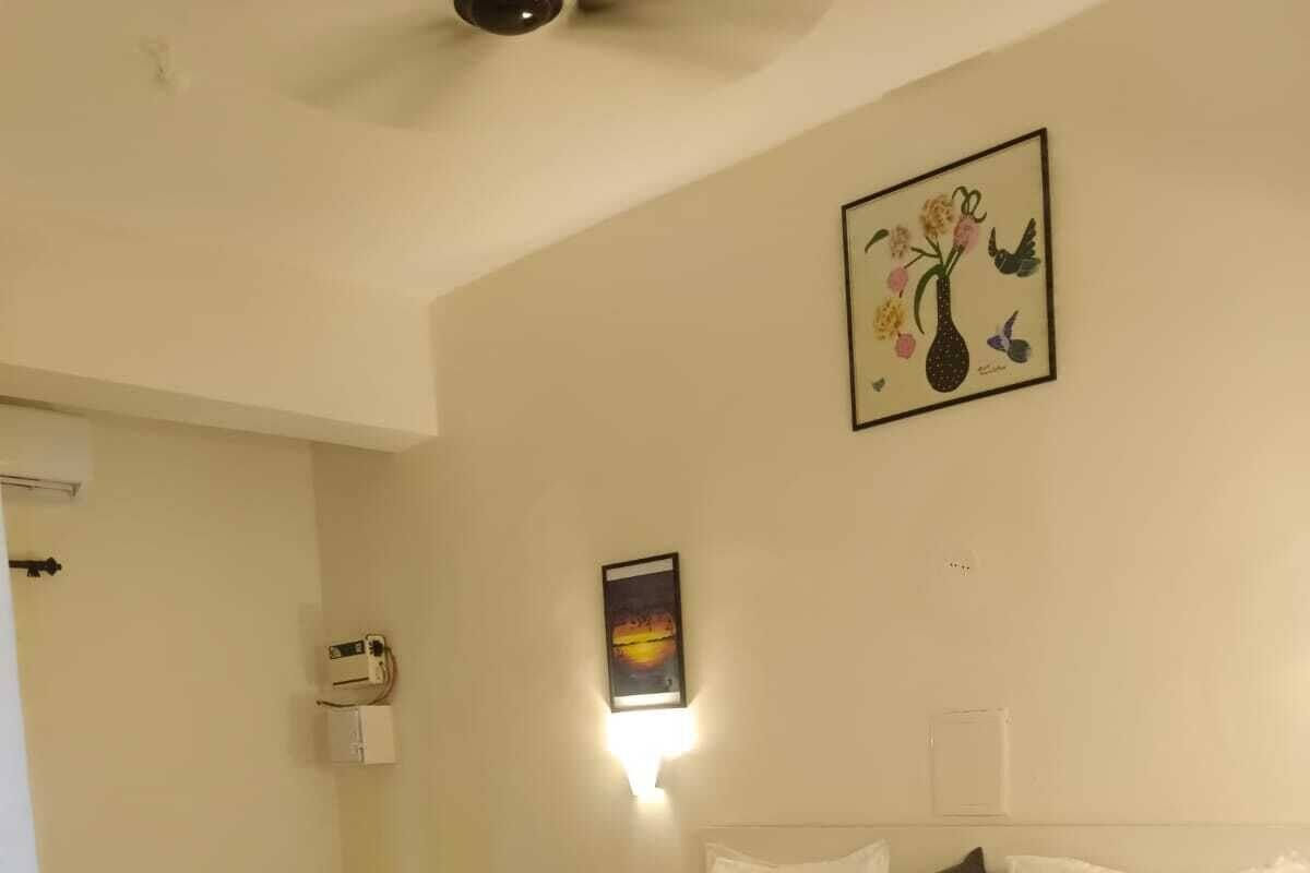 Ένα διπλό κρεβάτι με λευκά σεντόνια, ένα κομοδίνο, ένα φωτιστικό τοποθετημένο στον τοίχο και μια κορνιζαρισμένη εικόνα πάνω από το κρεβάτι.