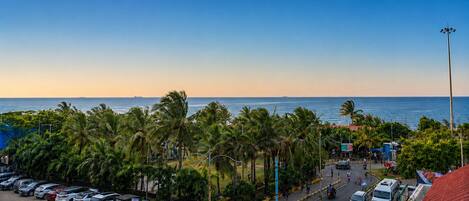 A coastal parking area with vehicles, palm trees, and a view of the sea.