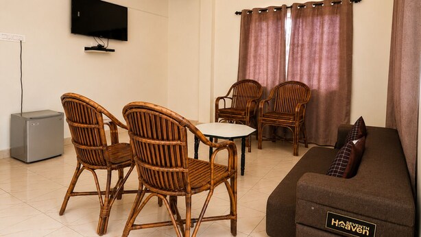 A living room with a sofa, two chairs, a small table, a television, and a refrigerator. - Holiday Beach Resort (Candolim)