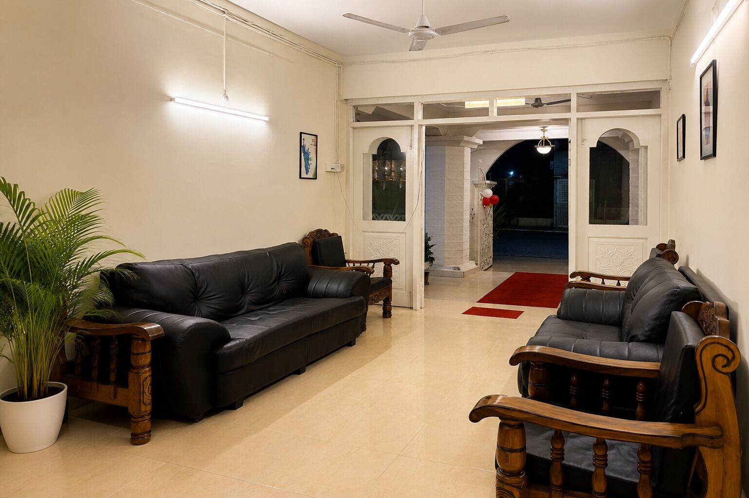 A living room with a black leather sofa, a wooden armchair, and a potted plant.