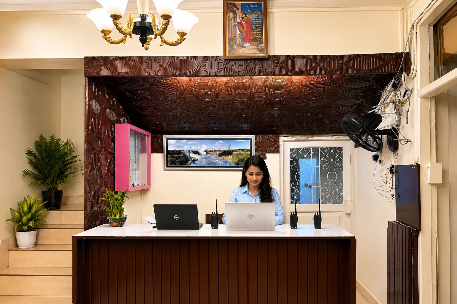 Un comptoir d’accueil avec deux ordinateurs portables, un tableau encadré et un lustre.