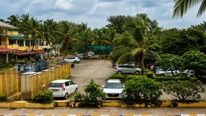 A parking lot with several cars, surrounded by palm trees and buildings. - Holiday Beach Resort (Candolim)