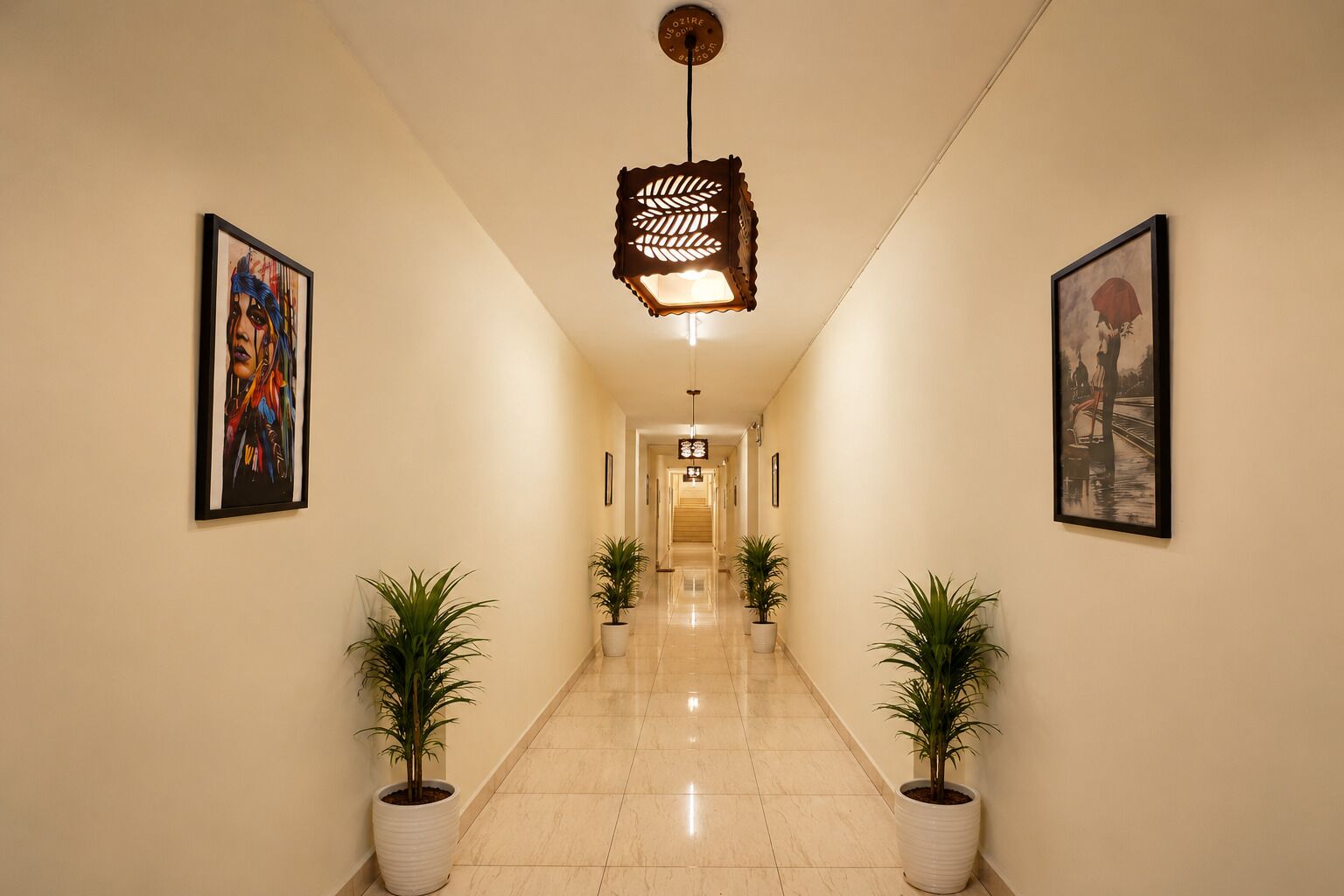 Un couloir doté d’un plancher poli, de plantes en pot, d’œuvres d’art encadrées et d’un luminaire décoratif au plafond.