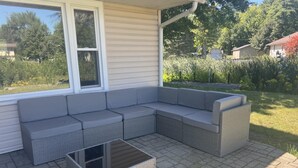 Un patio techado con un sofá seccional gris y una mesa de centro cuadrada.