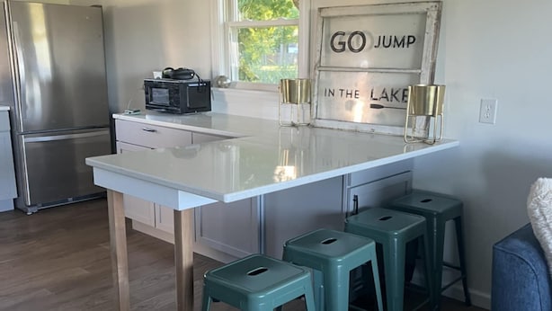 Una cocina moderna con un refrigerador de acero inoxidable, una encimera blanca y taburetes de bar color turquesa.