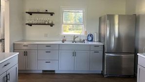 Una cocina moderna con armarios blancos, un refrigerador de acero inoxidable y una ventana con vistas a zonas verdes.