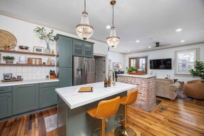 A modern kitchen with a central island, bar stools, and pendant lighting. - Promenade on Poplar- Brand New, Beautifully Decorated Cozy 2 Bedroom w/ King Bed (Columbus)