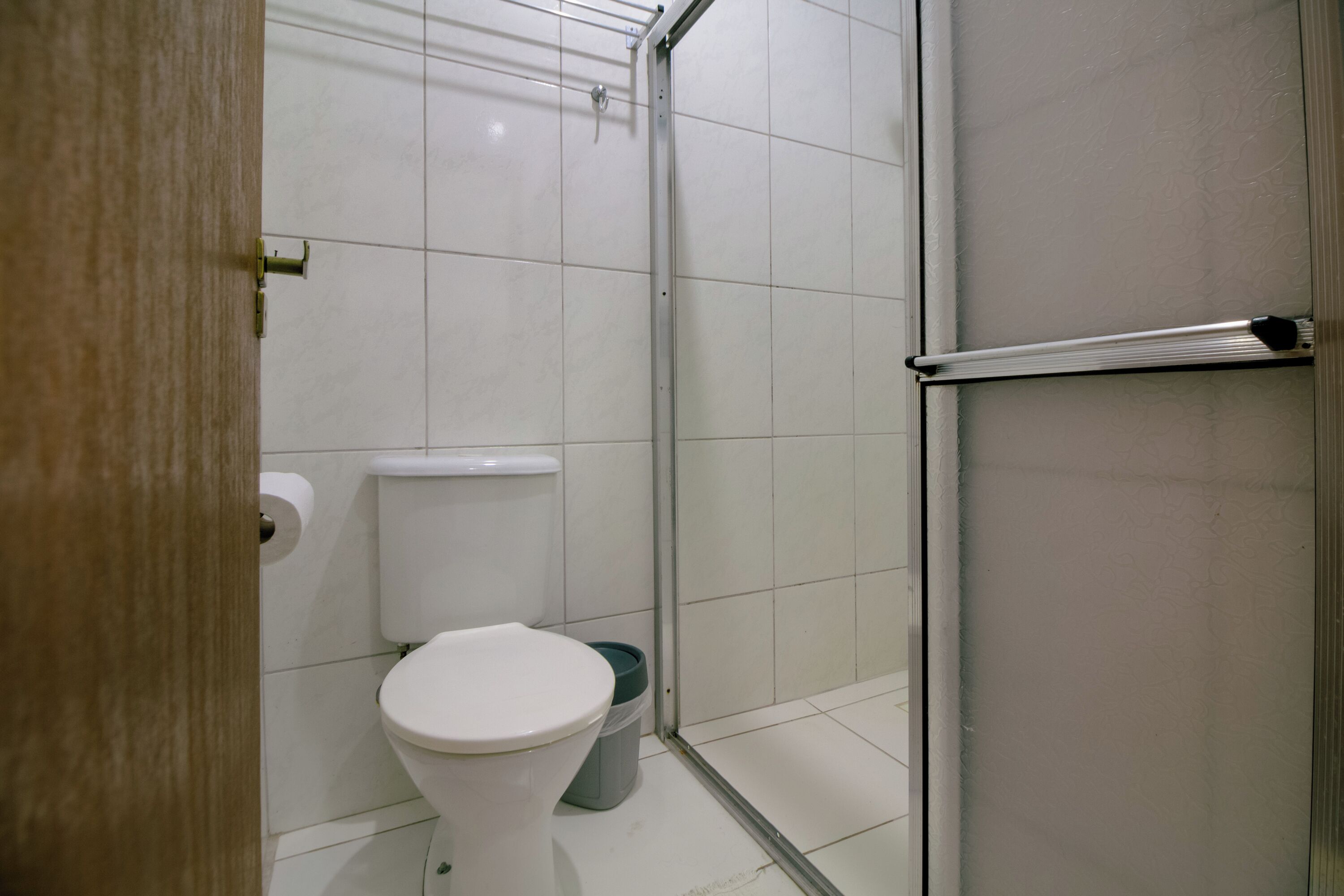 A bathroom with a toilet, a trash bin, and a glass shower enclosure.