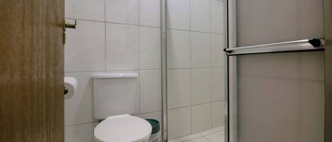 A bathroom with a toilet, a trash bin, and a glass shower enclosure.