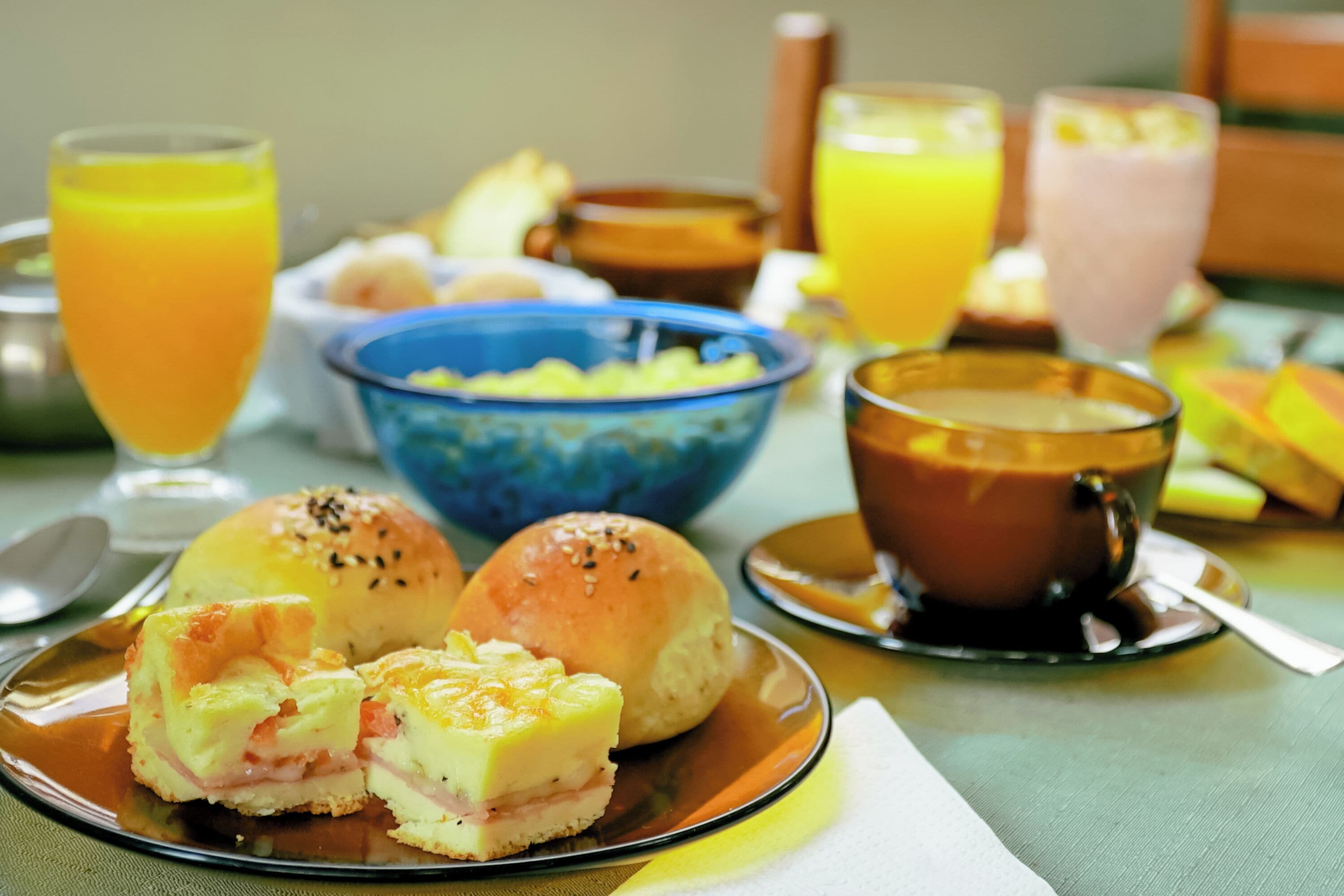 Una mesa de desayuno con un plato de comida, un bol de fruta y dos vasos de zumo de naranja.