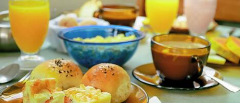 Una mesa de desayuno con un plato de comida, un bol de fruta y dos vasos de zumo de naranja.