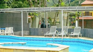 Piscina con bordes azulejados y una zona de estar cubierta con sillas.