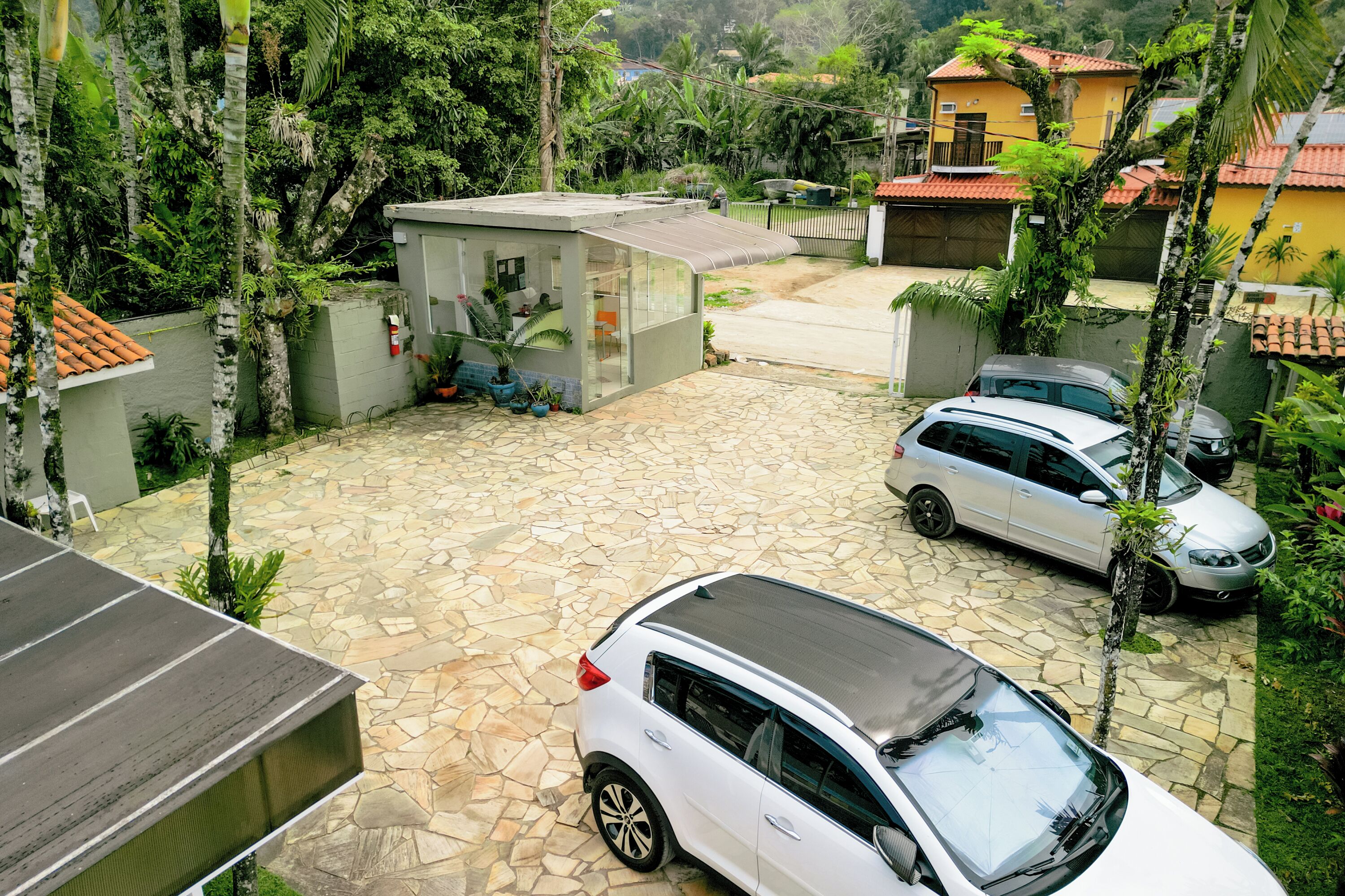 Zona residencial con un camino pavimentado, coches aparcados y un pequeño edificio con techo inclinado.