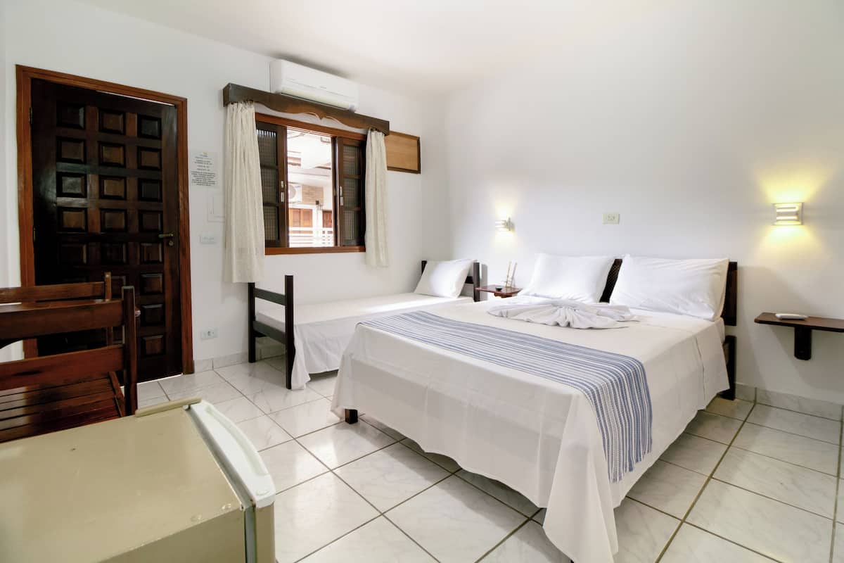 A hotel room with two beds, a wooden chair, a small table, and a window with curtains.
