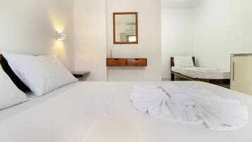 Quarto de hotel com uma cama grande, uma mesinha de cabeceira, um espelho e uma pequena mesinha com uma luminária.