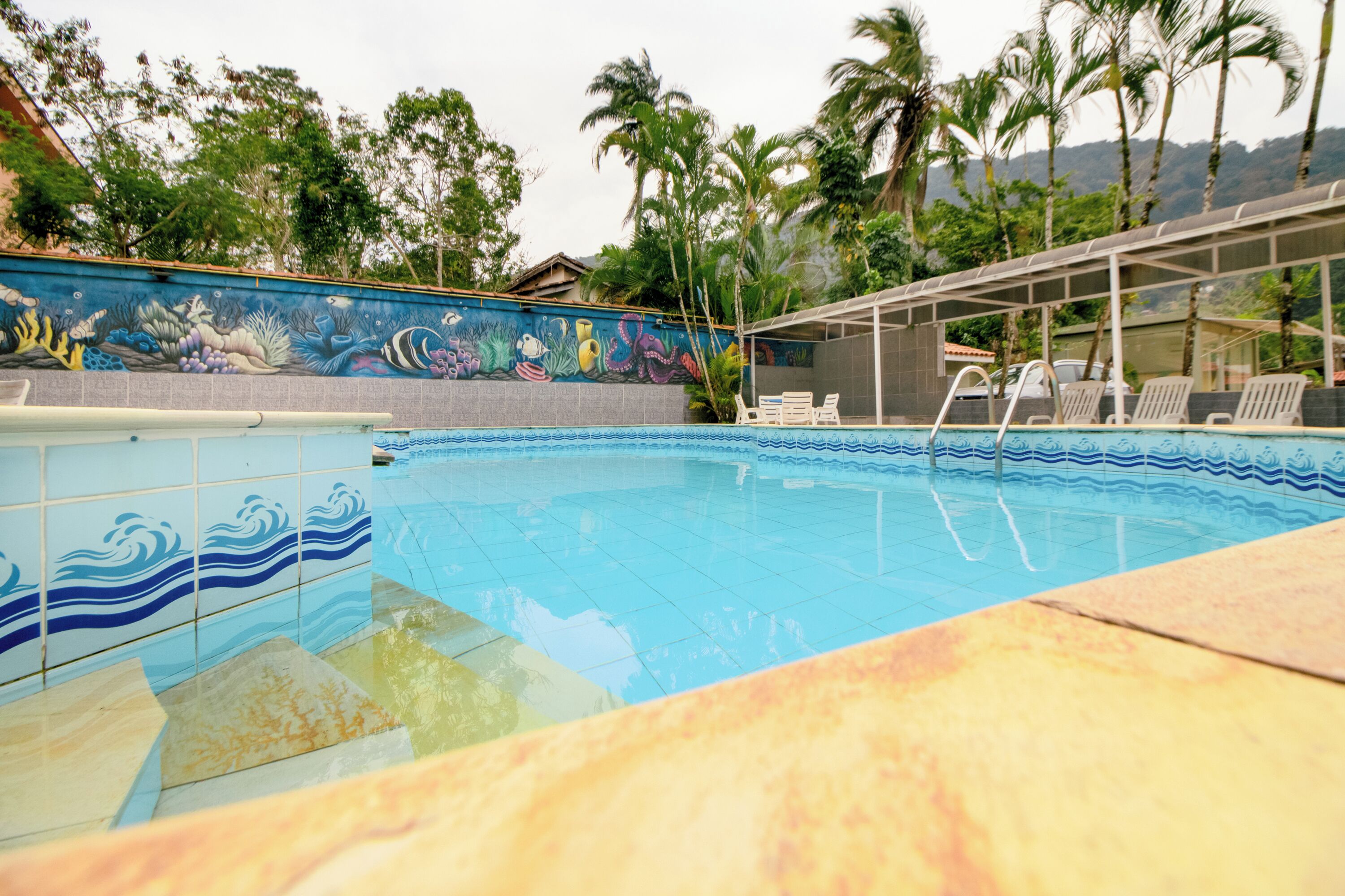 Uma piscina com bordas azulejadas, espreguiçadeiras e um mural com vida marinha.