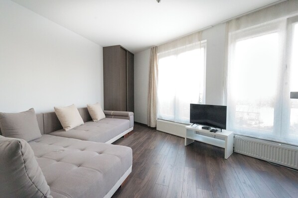 Relax in comfort with a sofa set facing a city view, complemented by a sleek entertainment unit and flat-screen TV.