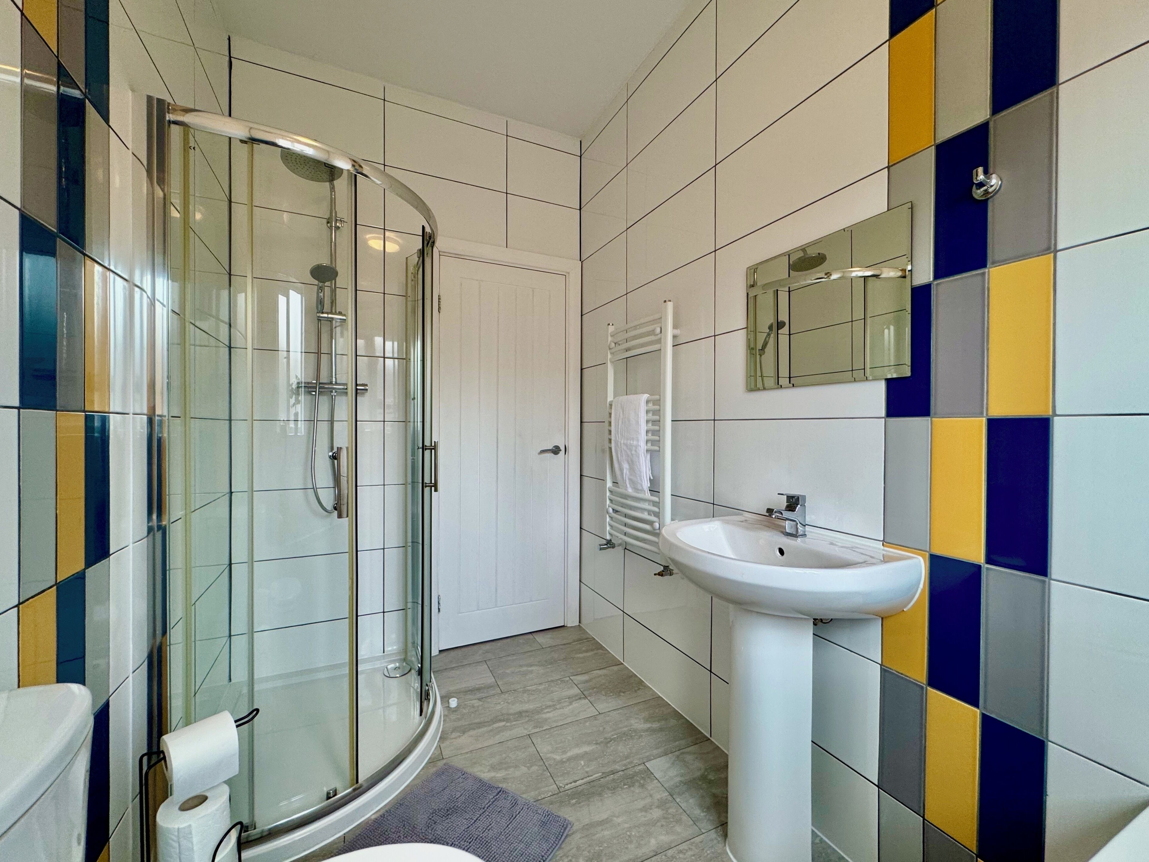 A modern bathroom with a glass shower enclosure, a white sink, and a tiled floor.