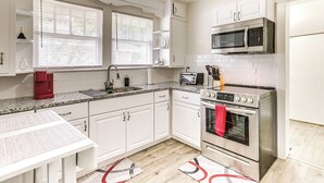 A modern kitchen with white cabinets, a granite countertop, a stainless steel oven, a microwave, and a red kettle. - Newly Renovated Birmingham Home: 7 Mi to Dtwn! (Birmingham)