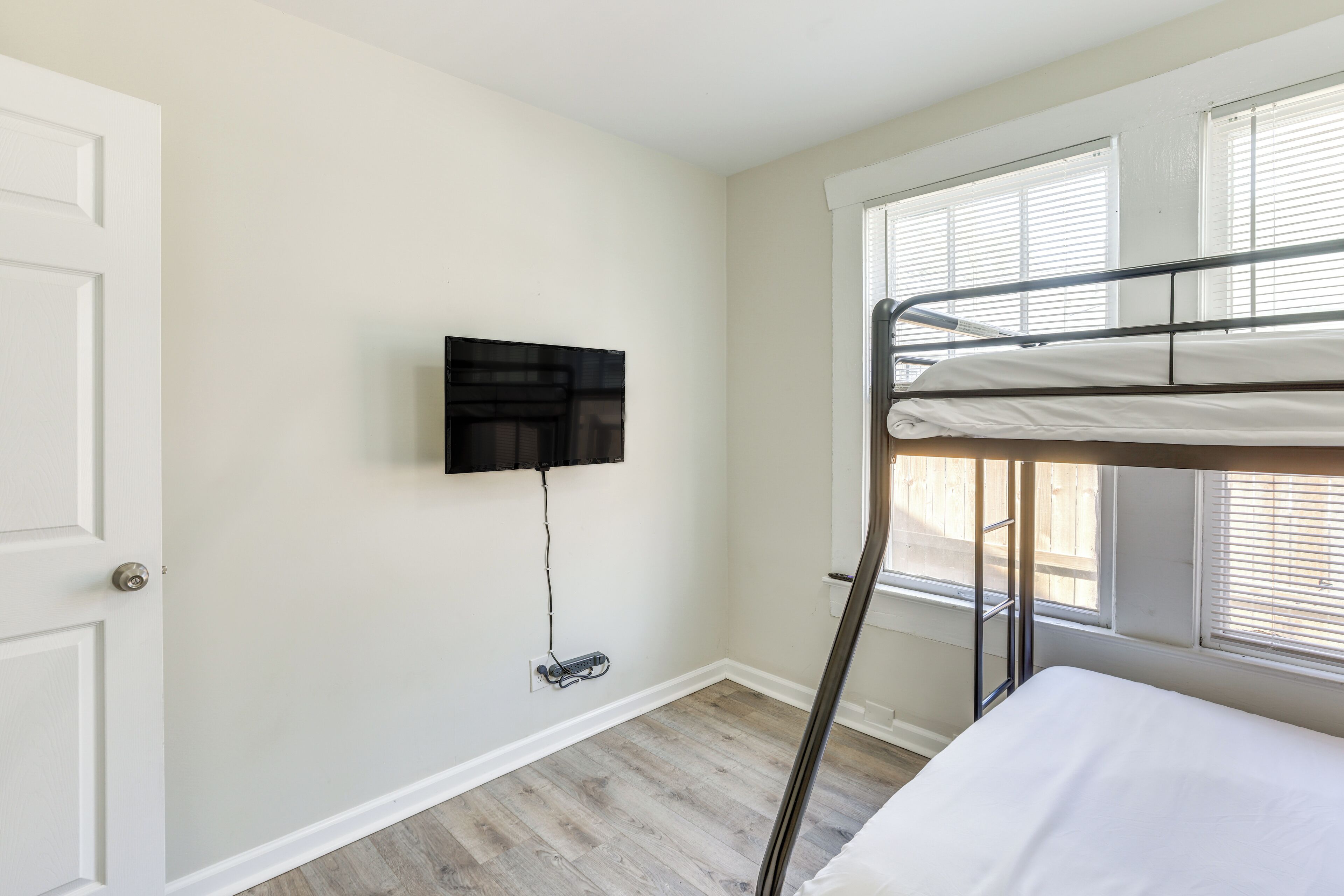 Een kamer met een stapelbed, een aan de muur bevestigde televisie en een raam met zonwering.