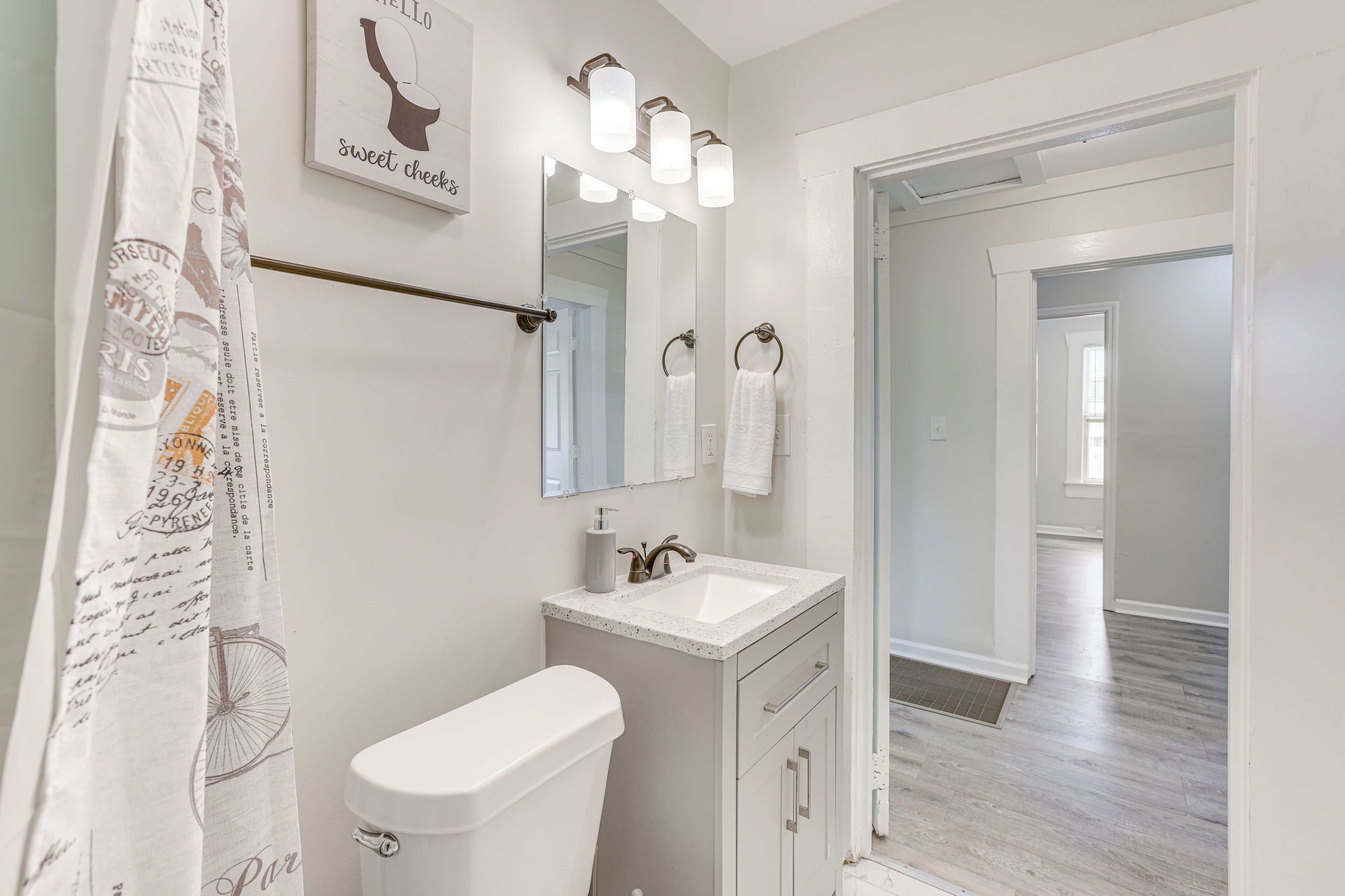 A bathroom with a toilet, sink, and mirror. There is a towel rack with two towels. The walls are white, and the floor is wooden.